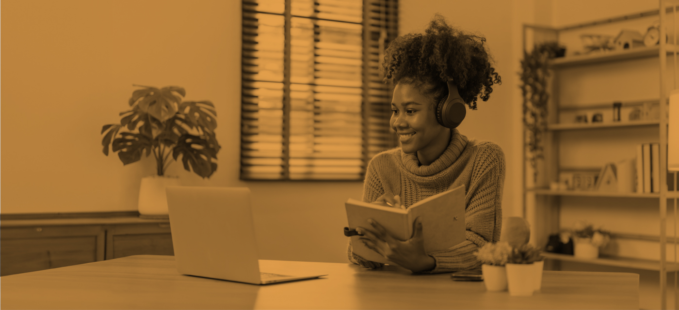 Student smiling while holding book and attending class remotely