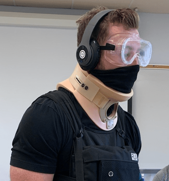 A physical therapy student in goggles, headphones, neck brace, and weighted vest to simulate challenges that elderly patients face.