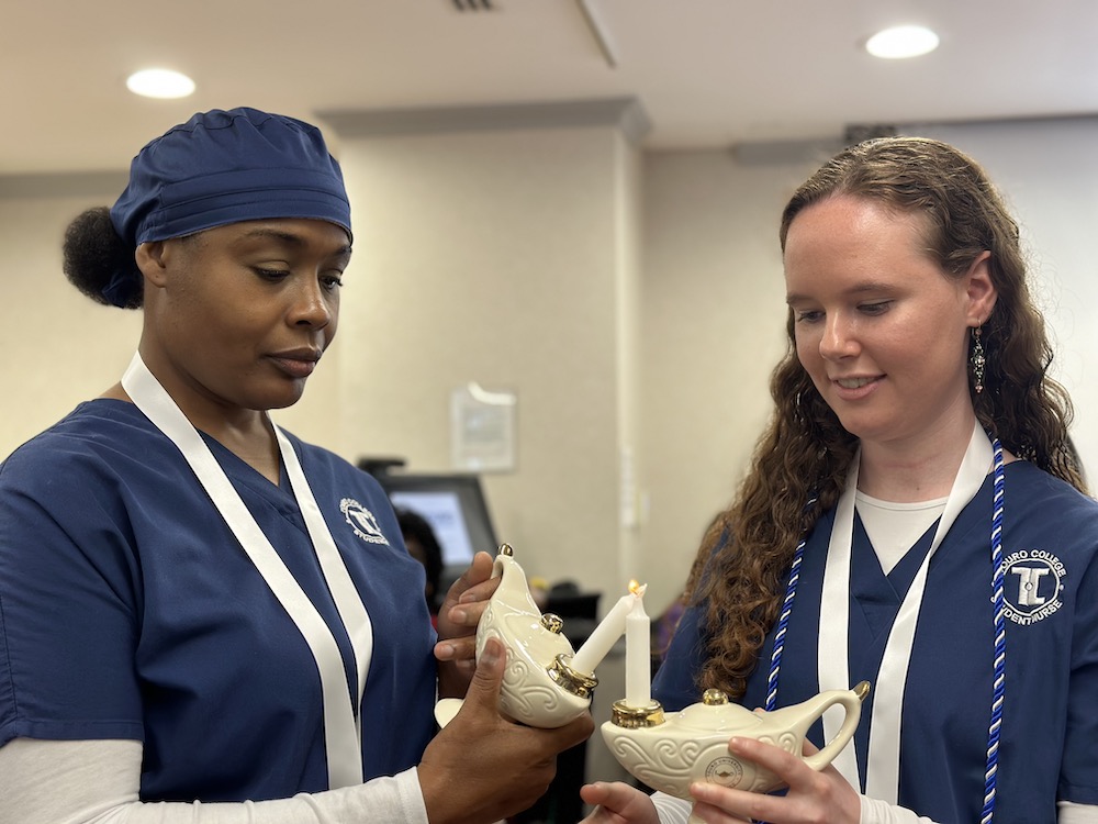 One nursing student lights the commemorative lamp of her fellow nursing student during a commencement ceremony.