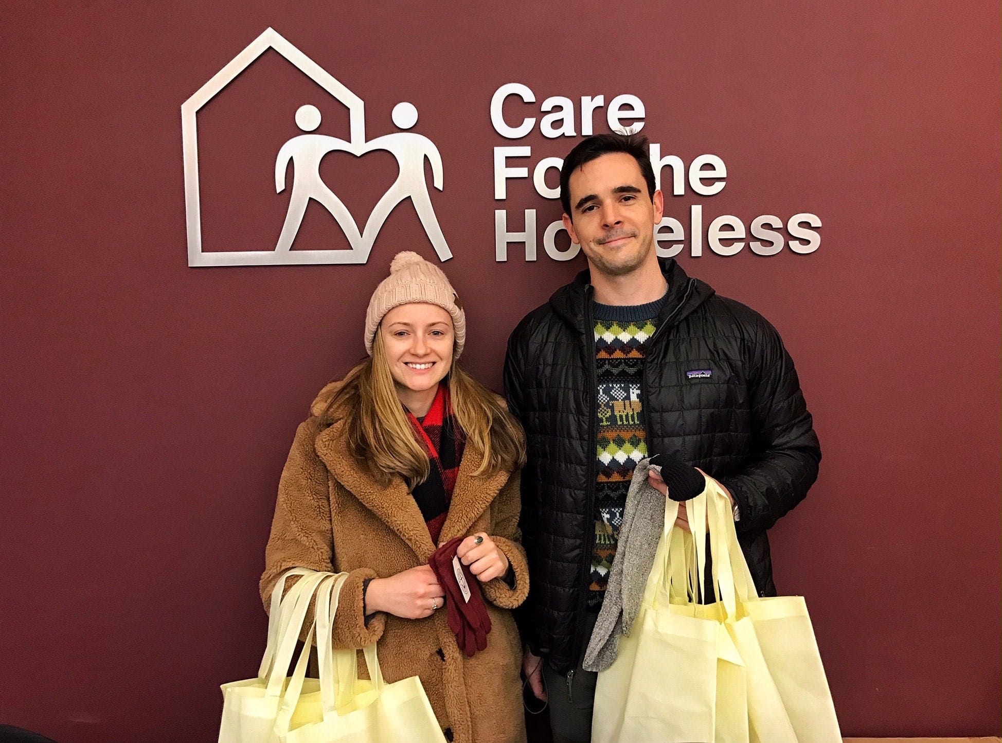 Cory Wright, right, holding the canvas tote bags in front of the \'Care for the Homeless\' sign.