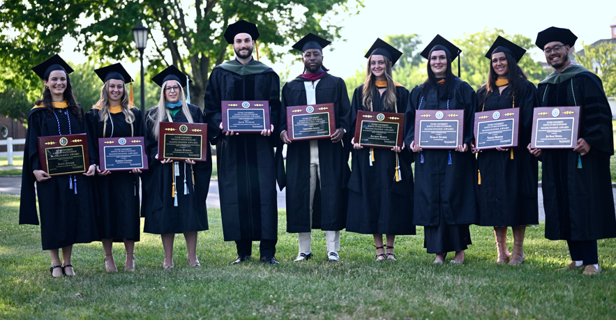 Eleven students in caps and gowns holding their awards.