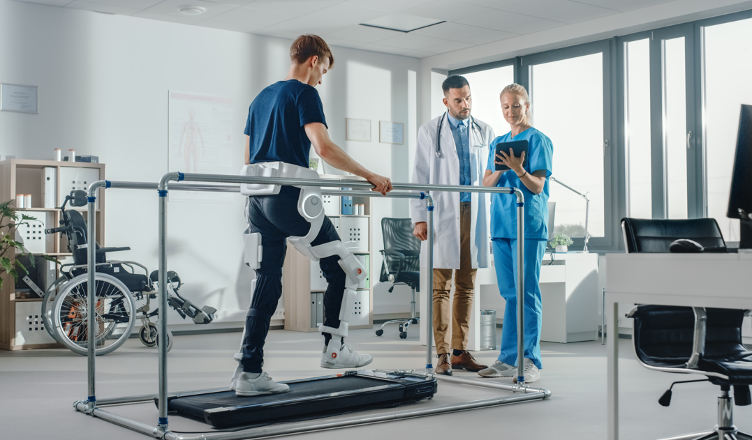Man on treadmill with physical therapist and doctor standing by and looking at tablet screen.