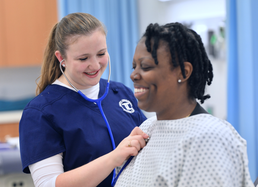 Female Touro nursing student examining a patient in a gown.